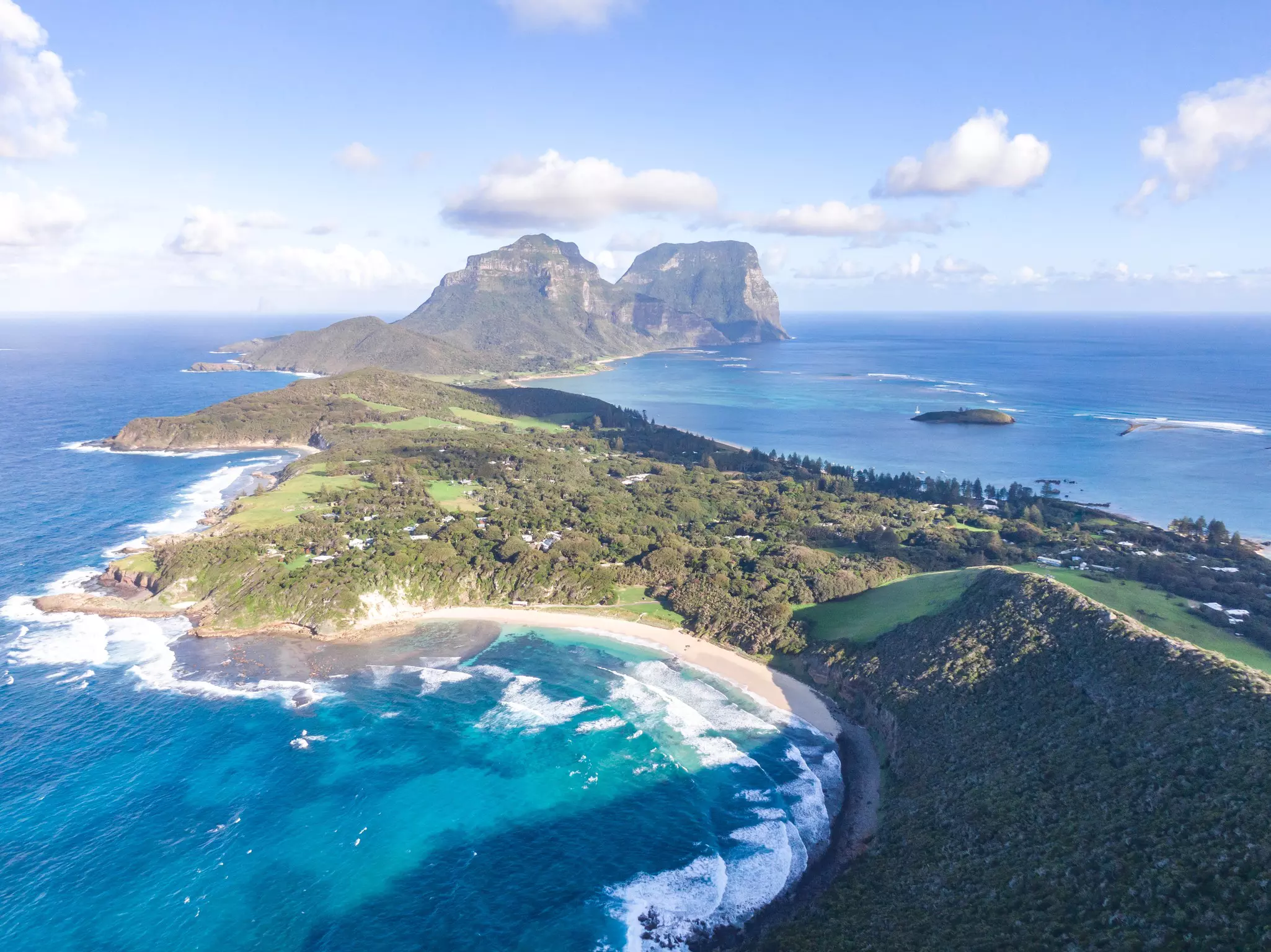 A drone view of an island with water lapping green shores