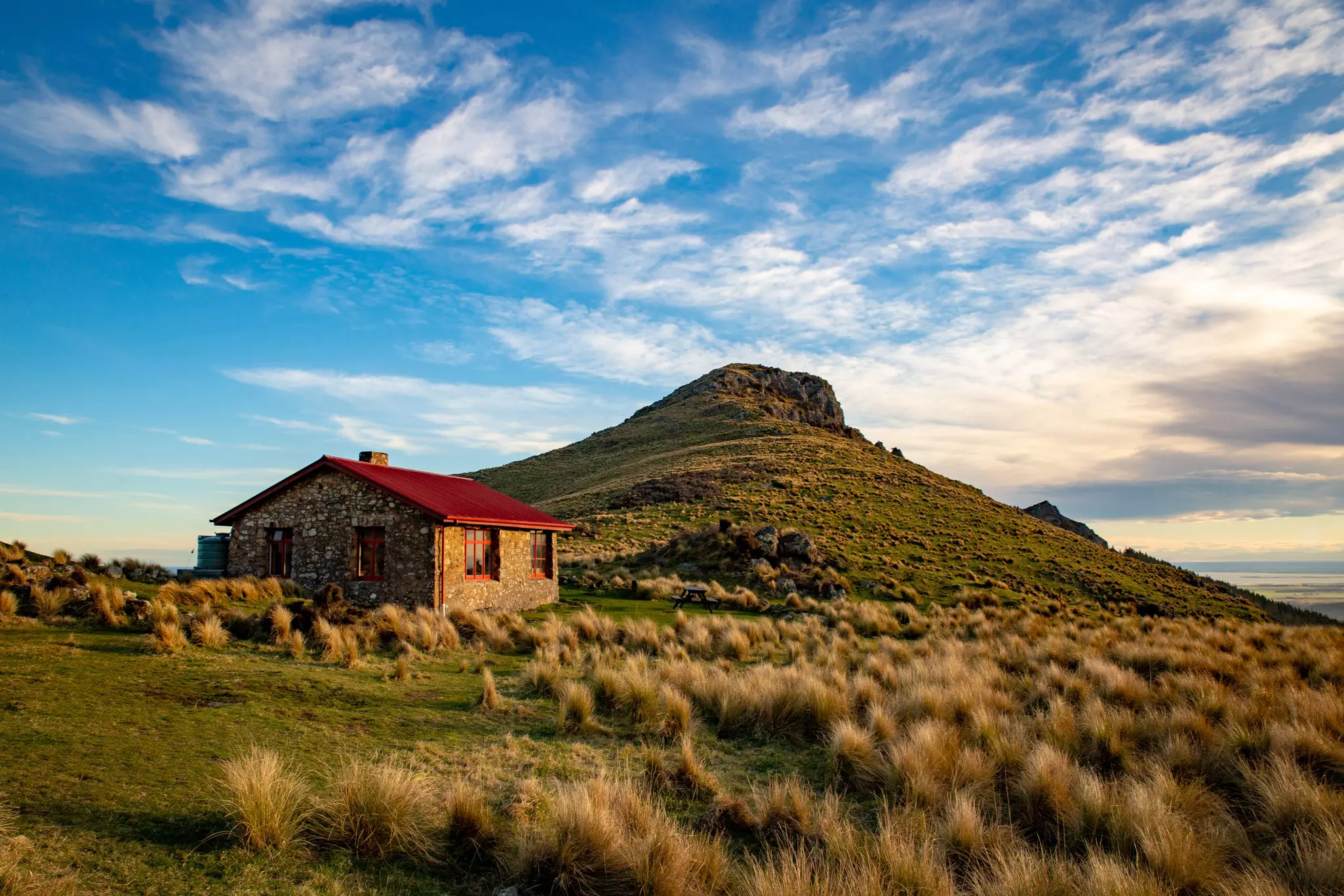A historic stone hut with a pointed red roof sits high on a ridge.