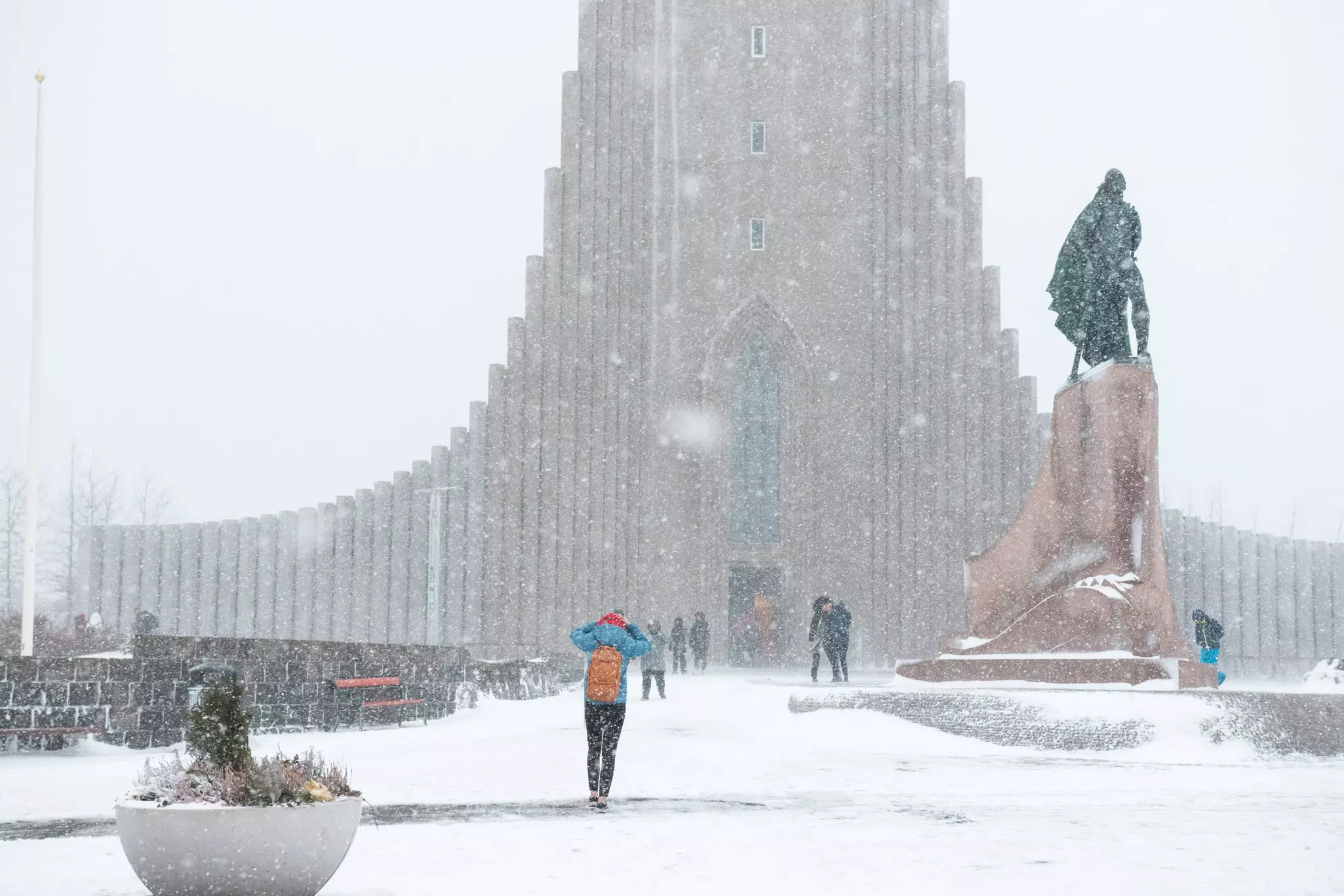 People walk in a blizzard past statues and toward the tower of a church.