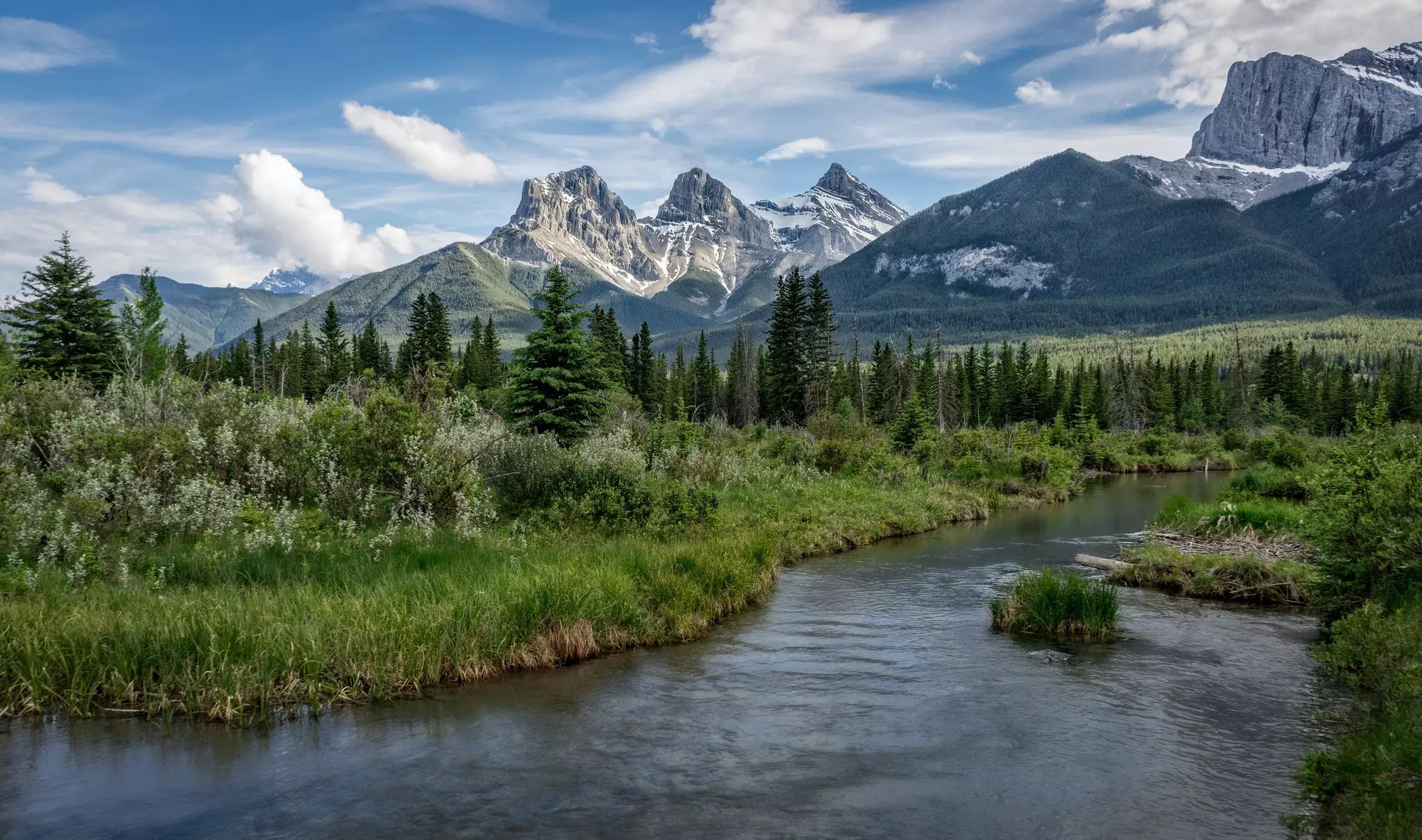 The Three Sisters mountains in Canmore, with trees and water nearby