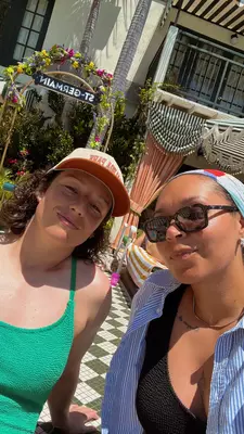 A selfie of two women smiling poolside on a sunny day.