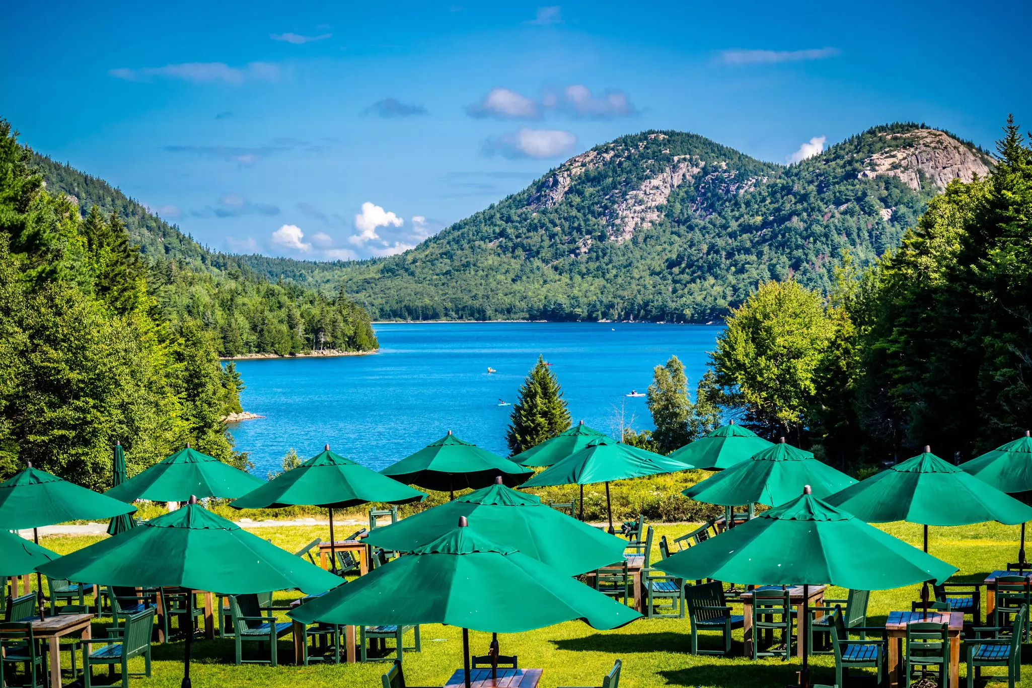 A vast lawn between a restaurant and a large lake surrounded by woodland on a sunny day; Jordan Pond House Restaurant, Acadia National Park, Maine. 