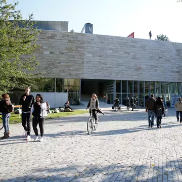 People walk and cycle past Kunsthal Rotterdam on a sunny day.