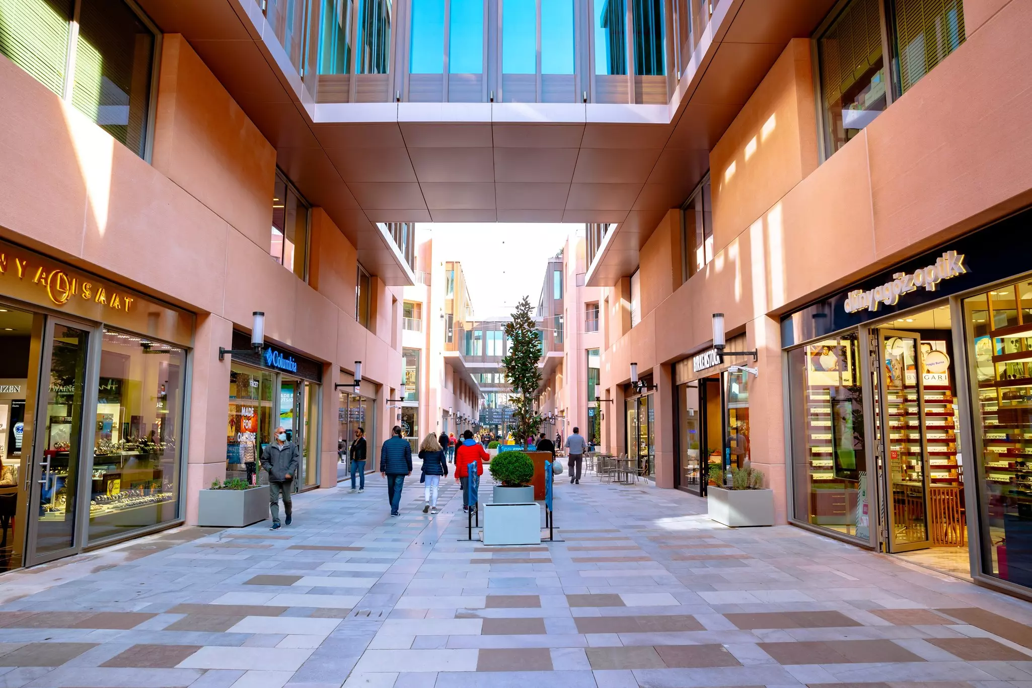 People walk down an avenue within an open-air shopping mall with stores either side of them.
