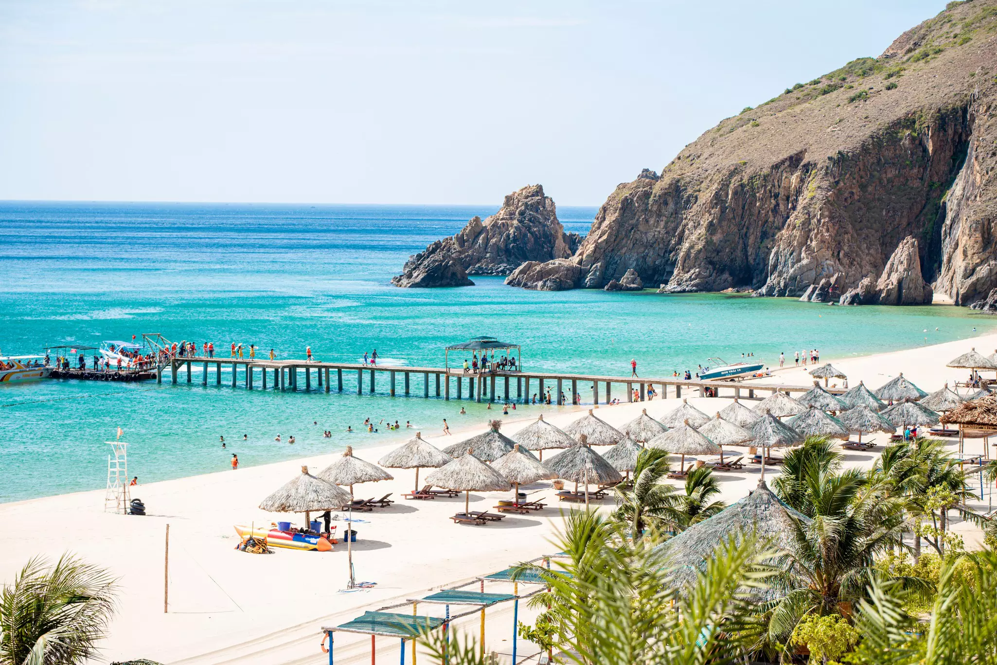 A white-sand beach with thatched sunshades and a wooden jetty.