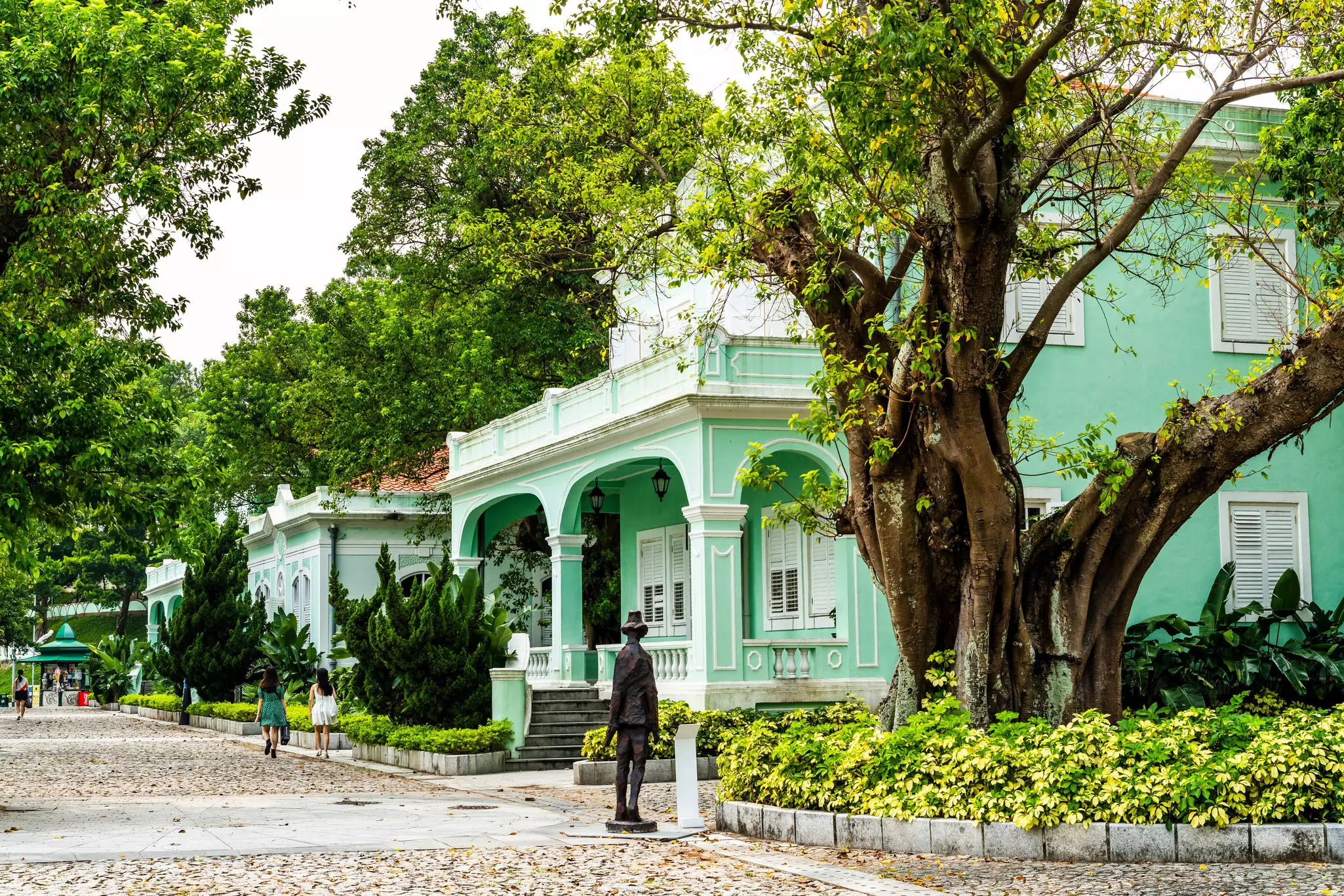 Green-painted villages stand side by side on a city street with old trees and greenery.