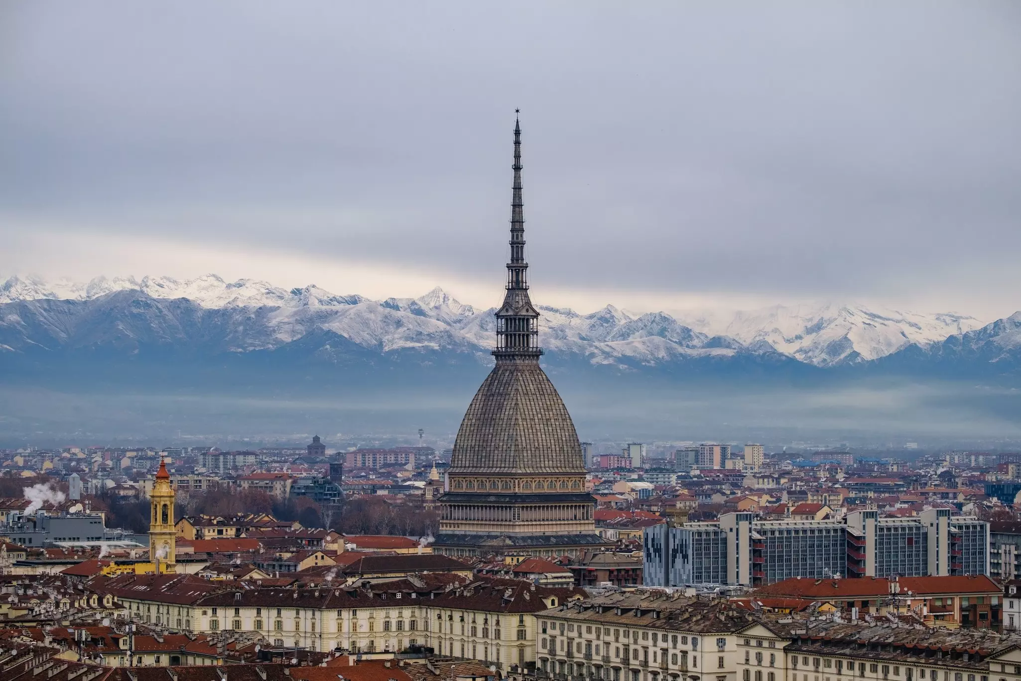 A large domed tower rises above a cityscape with snow-topped mountains in the background.