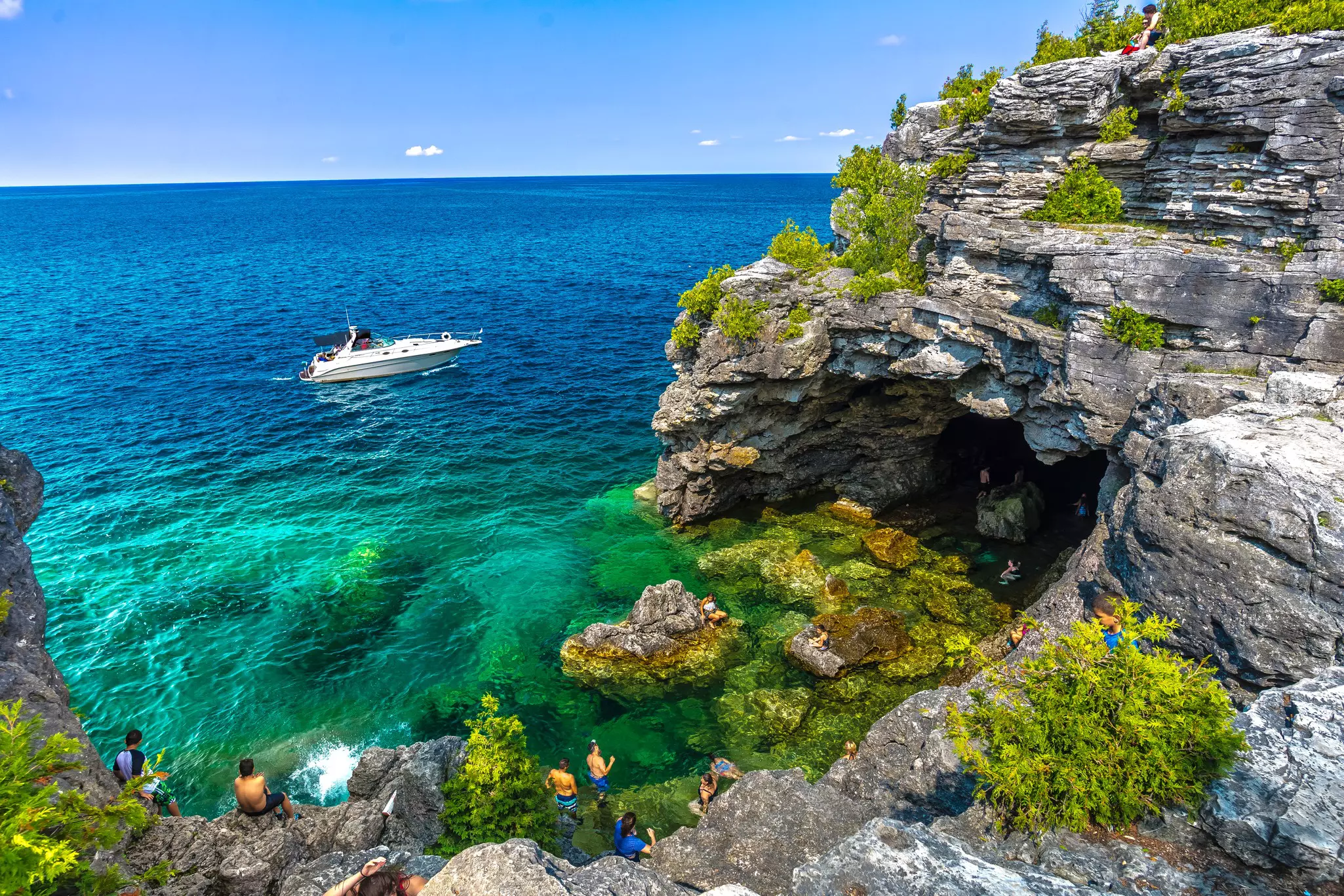A view of a swimmers in a cove framed by rocky cliffs as a boat is moored just offshore, Bruce Peninsula National Park, Ontario