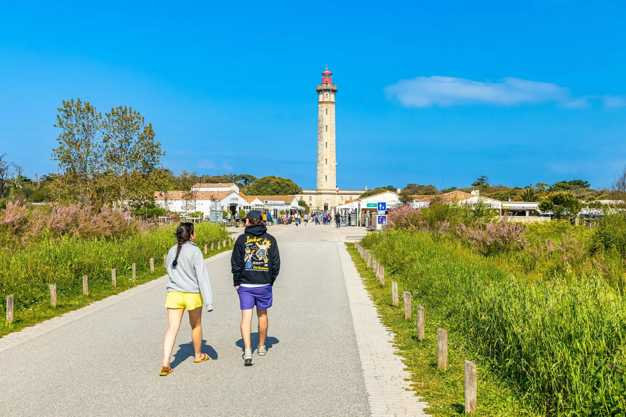 Two young people walking on a path toward a lighthouse