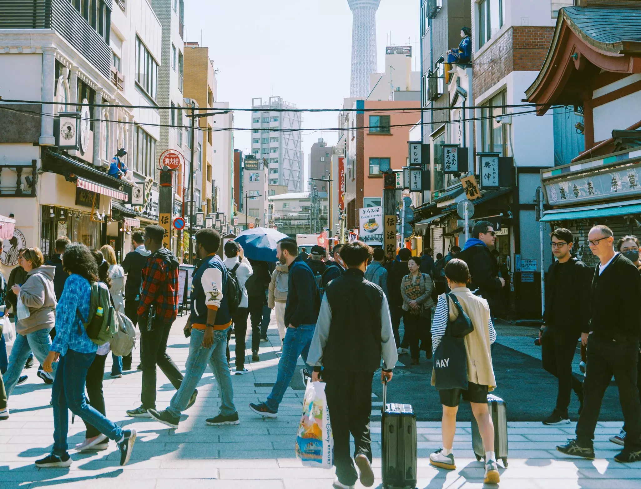 People wheeling bags down a busy shopping street in a city