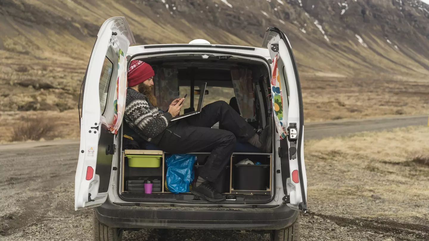 Iceland, man sitting in van using smartphone and laptop