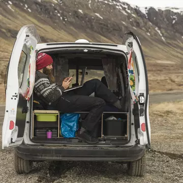Iceland, man sitting in van using smartphone and laptop