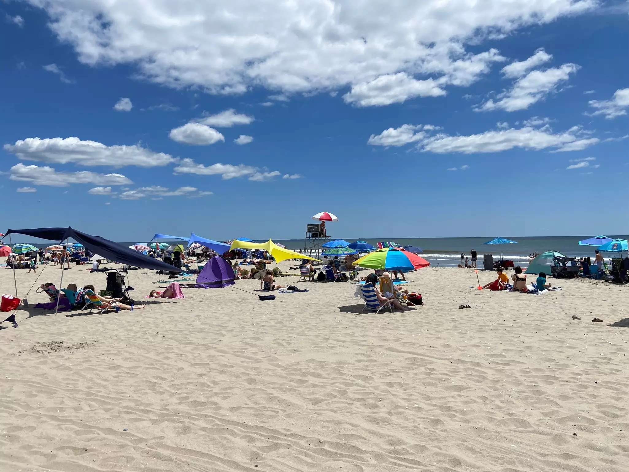 A beach with people under colorful sun umbrellas and tents, and a lifeguard near the water