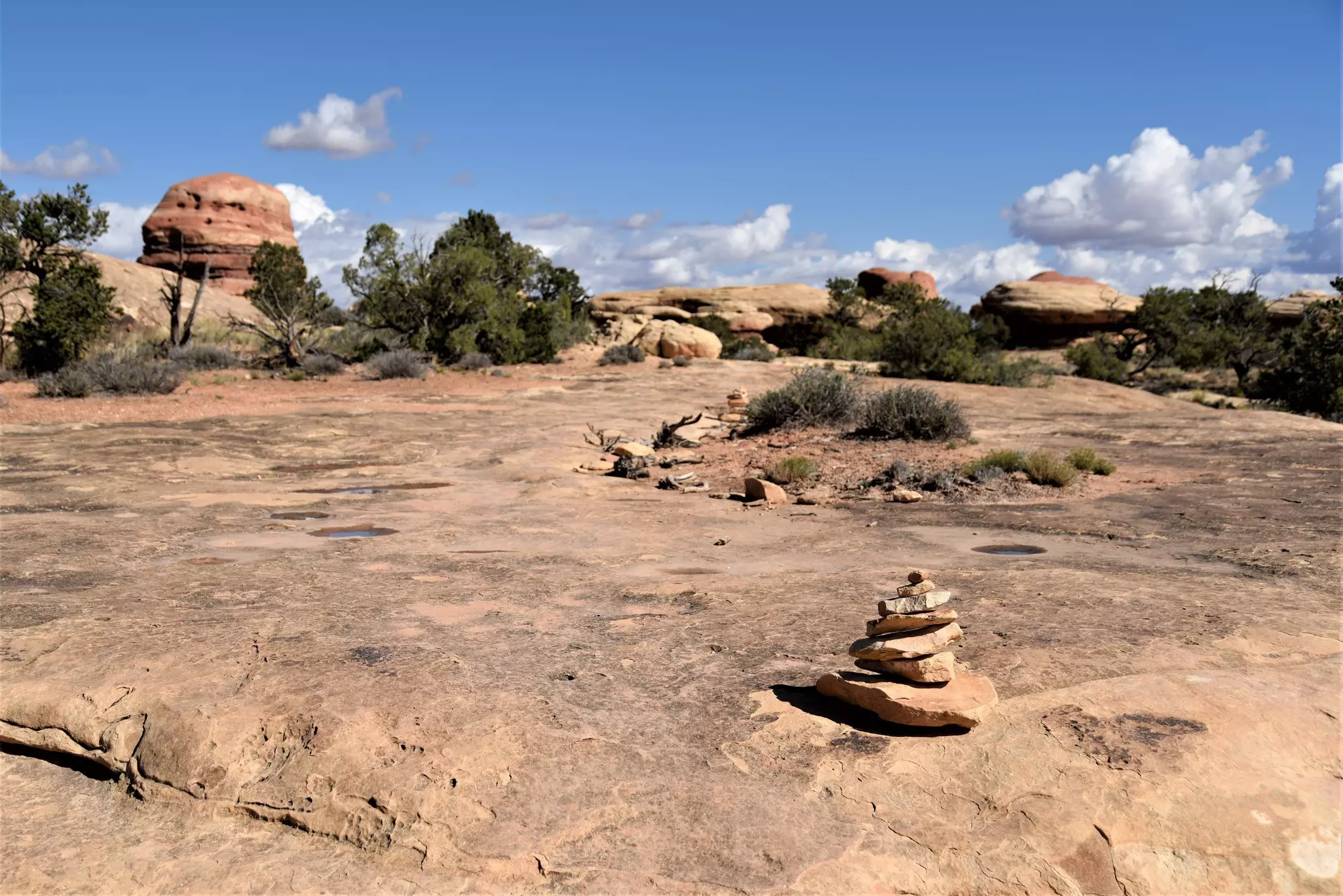 Small stacks of reddish rocks mark the trail across a rocky plateau.