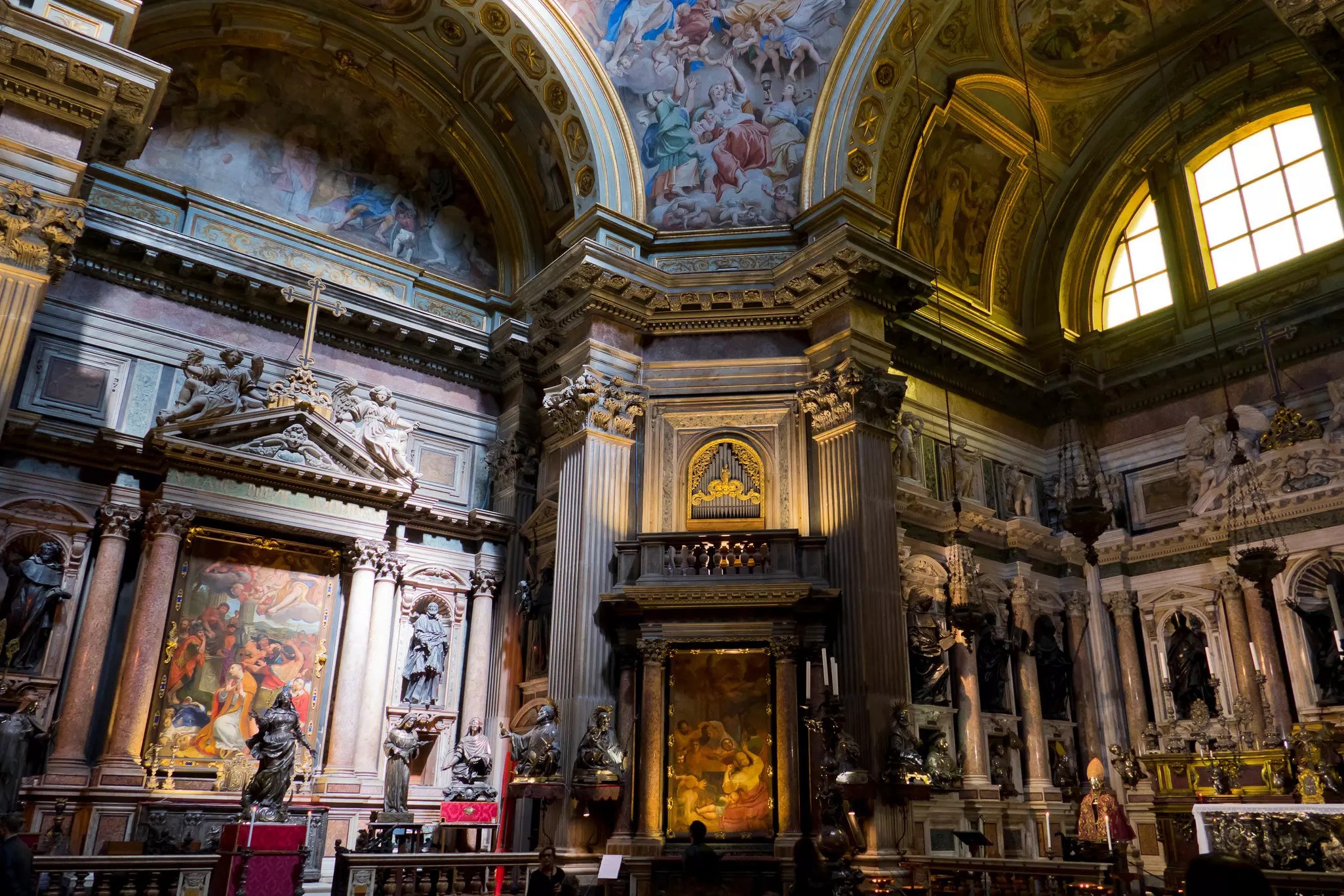An elaborate chapel in a church features carved columns, frescoes depicting religious scenes and statues of sains.