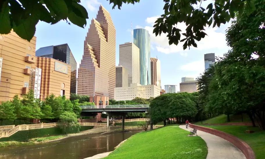 Wide shot of Houston's modern skyline and paved bicycle/walking path in Buffalo Bayou Park on a summer afternoon