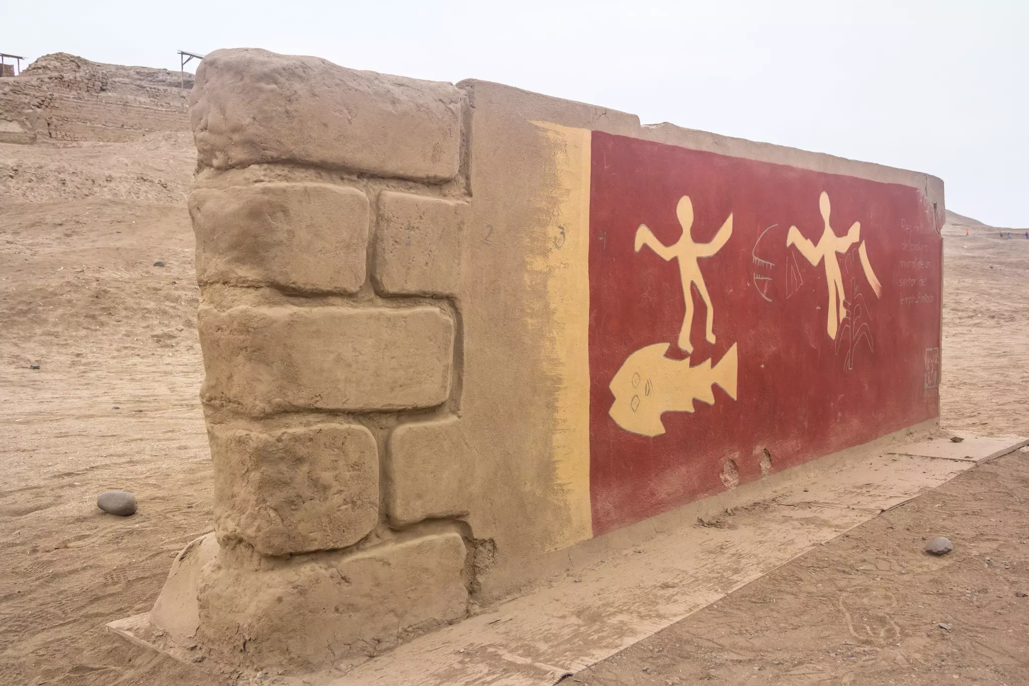A reconstructed fragment of an ancient wall and petroglyphs depicting figures and a fish in the desert