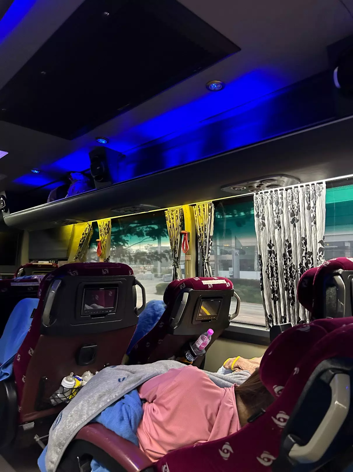 People sleep under blankets on rows of reclining seats on a coach at night. 