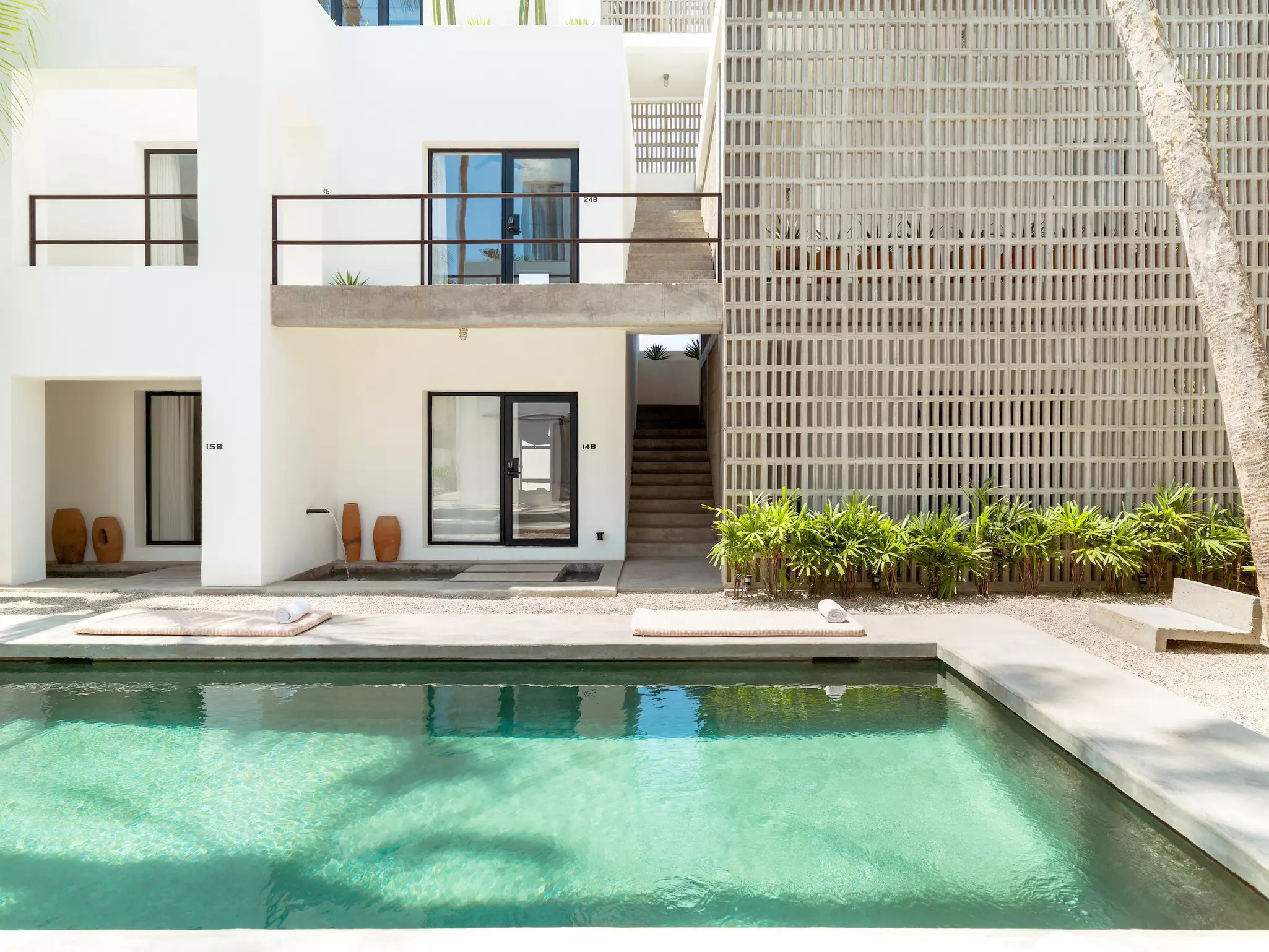 A pool is in front of a white building with a black door and small shrubs