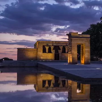 An ancient stone temple and gateways reflected in a still pool at dusk.