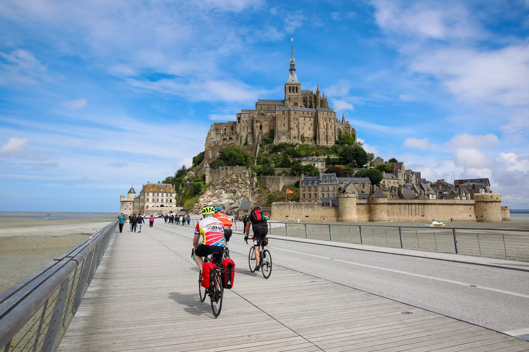 Cyclists on a boardwalk near a towering seafront abbey
