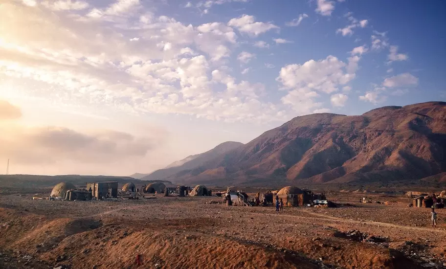Domed nomad huts on a stony desert plain below reddish mountains, Djibouti