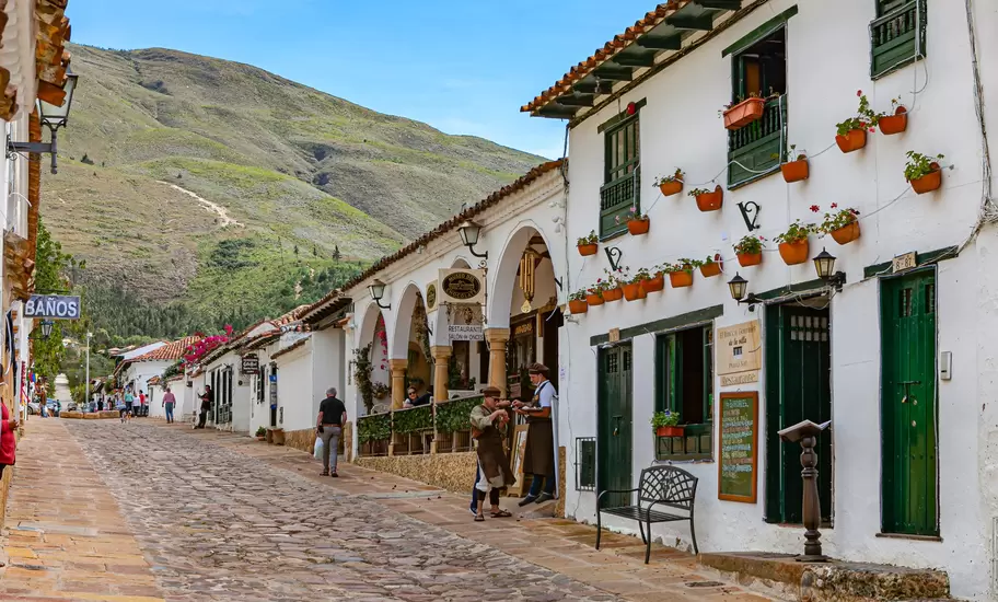 A cobblestone street of whitewashed colonial buildings with green balconies and flowerpots in Villa de Leyva, Colombia