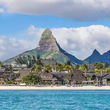 A gorgeous sandy beach lined with palm trees and a resort, backed by a huge pointed mountain 