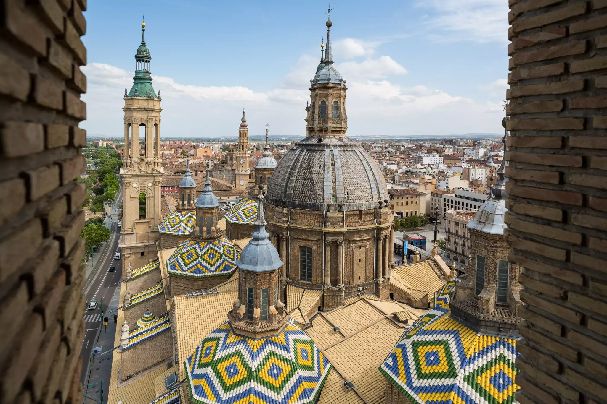 Roof and central dome of a vast cathedral building, with ornate tiled patterns, in the center of a city.