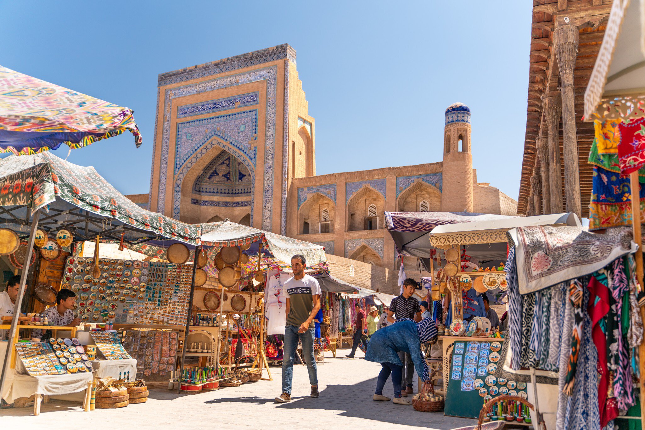Man walking through an outdoor market lined with stalls of textiles and other products
