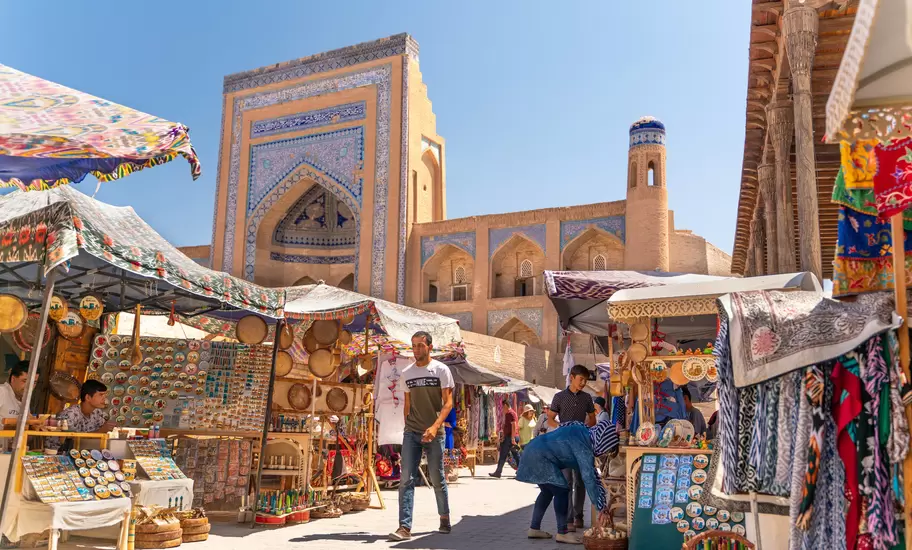 Man walking through an outdoor market lined with stalls of textiles and other products