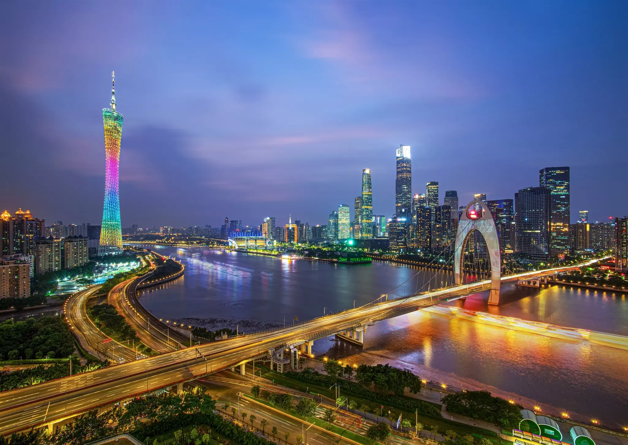 Night in a high-rise city with bridges, roadways and buildings lit up in bright lights and neon.