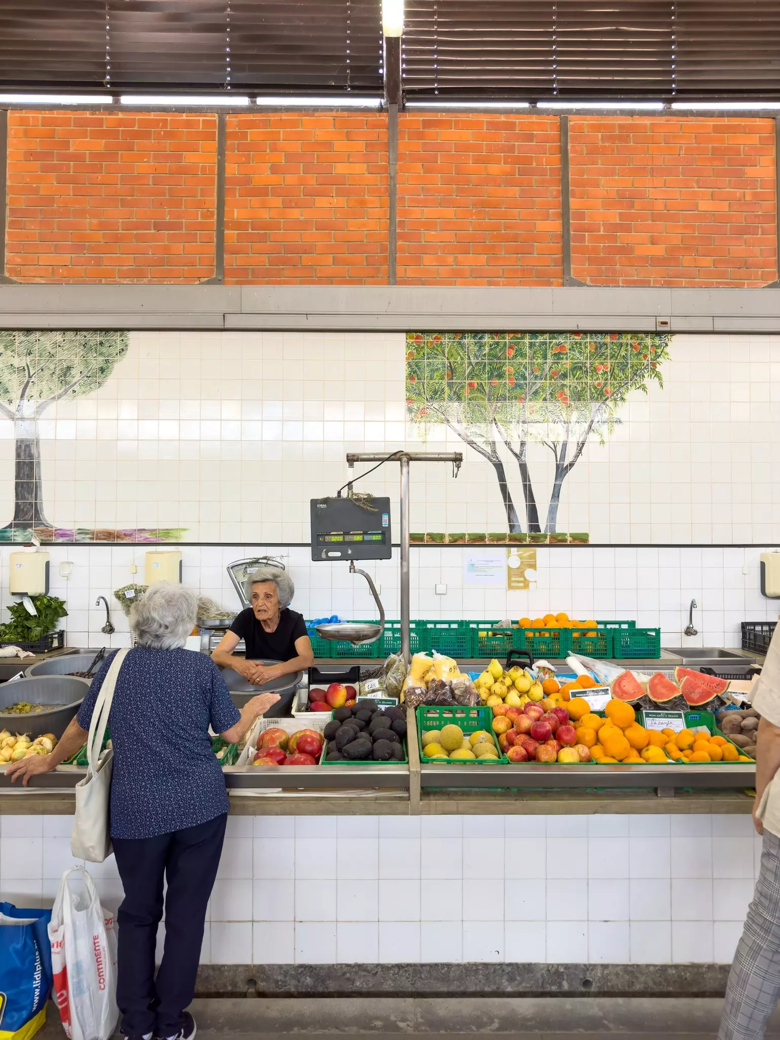 A server at a fresh fruit and vegetable stall in a market talks to a customer