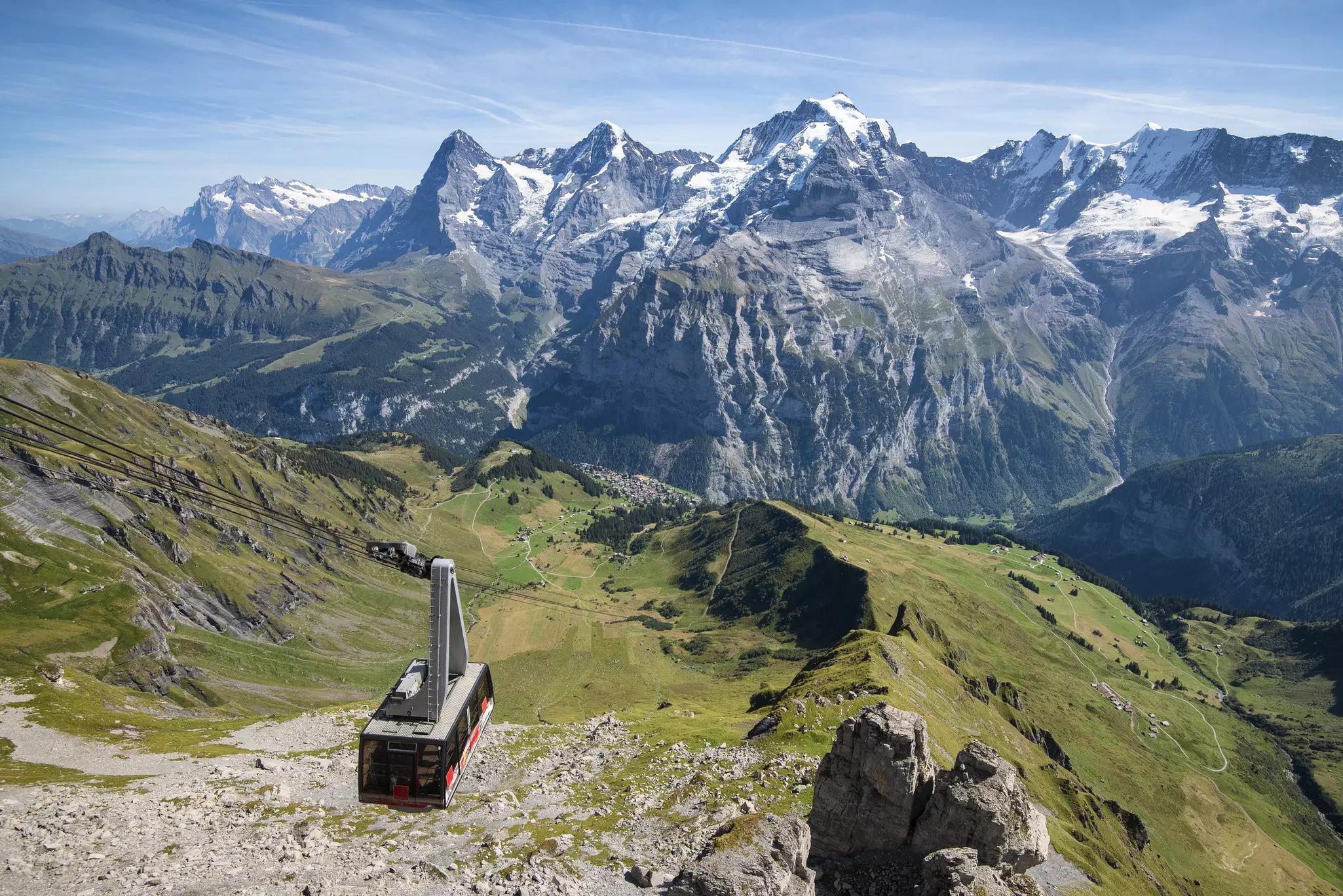 A cable car on a cableway in a vast mountain range on a sunny day.