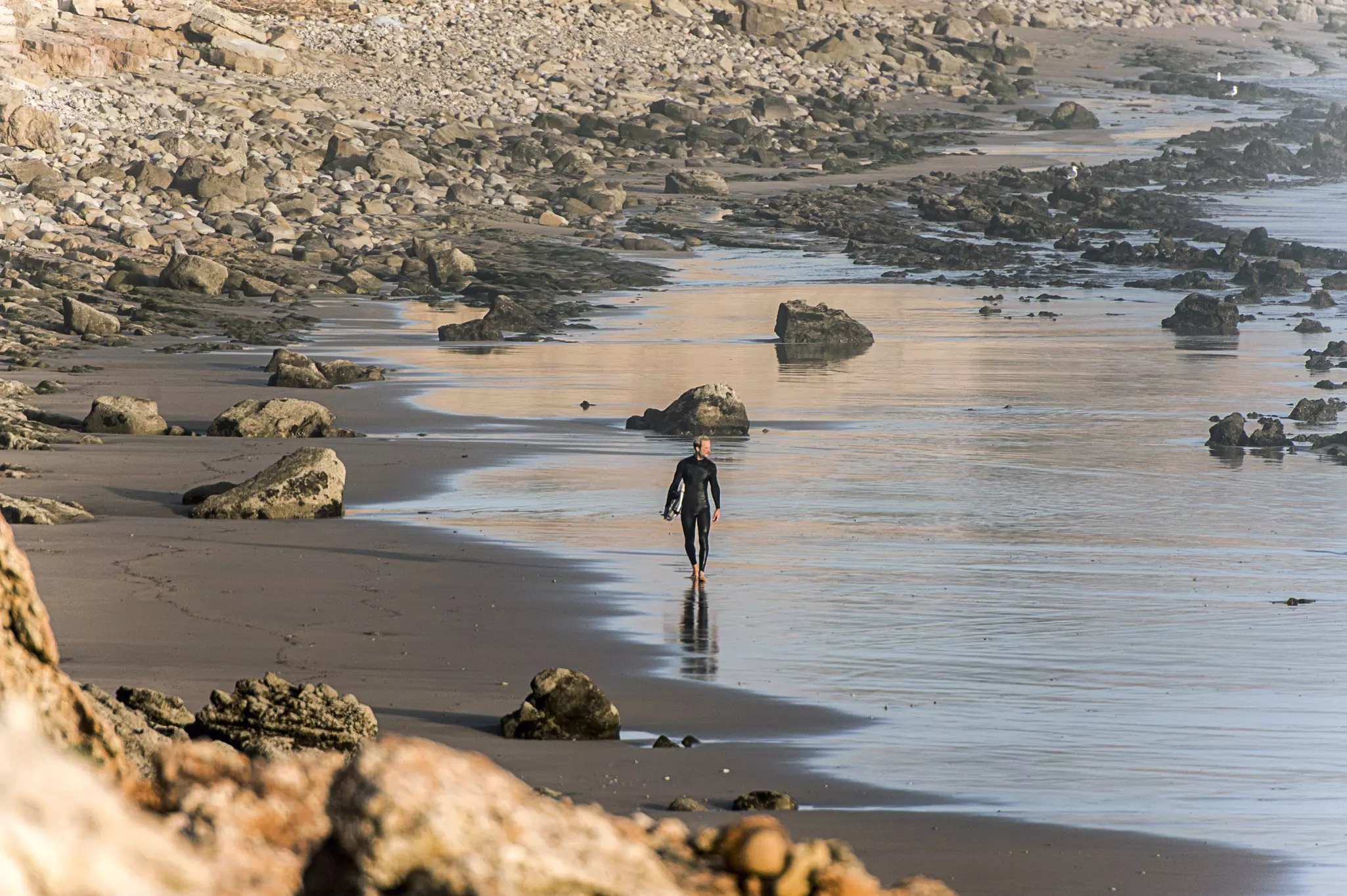 Surfer walking at rocky beach, Tamraght, Morocco