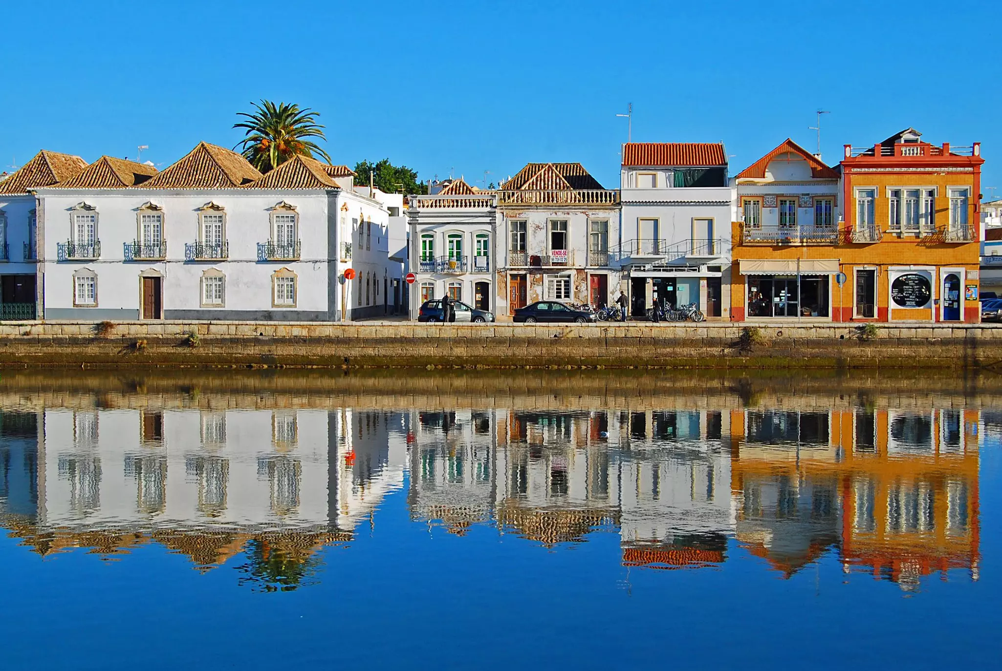 A line of white and yellow buildings reflected in blue water on a sunn day.