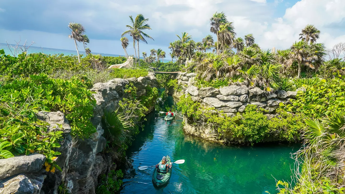 A person kayaking in a channel through rocky walls and green jungle at Xcaret in Playa del Carmen, Mexico