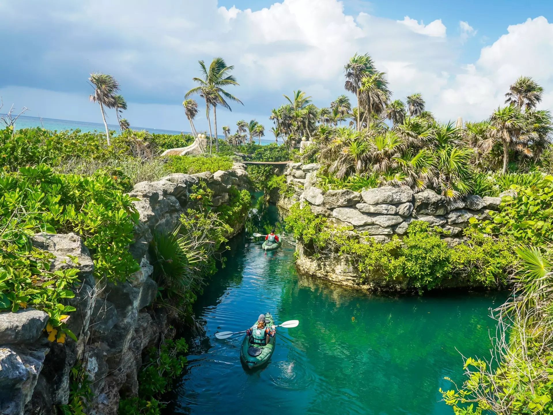 A person kayaking in a channel through rocky walls and green jungle at Xcaret in Playa del Carmen, Mexico
