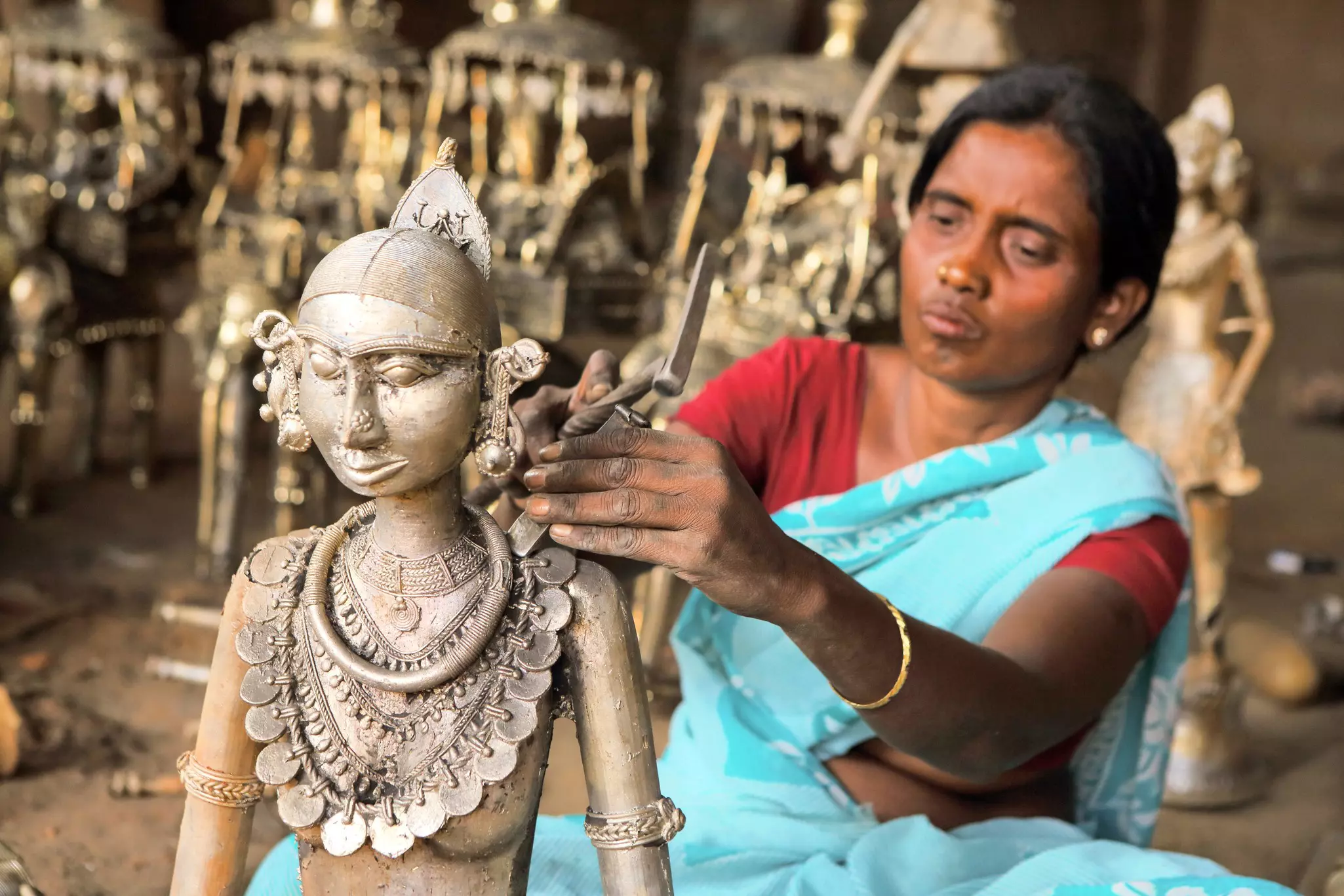 A tribal woman using hand tools to clean the bell-metal casting of female figure in a rural workshop.