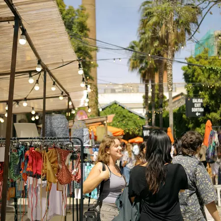 Two women chat by a clothing stall at an outdoor market