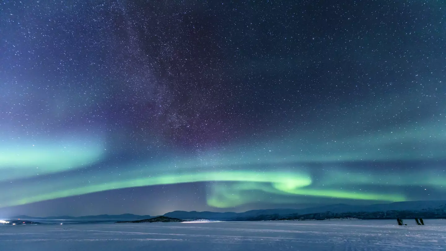 Green stripes of aurora borealis lights on a dark sky over a vast snowy field. 