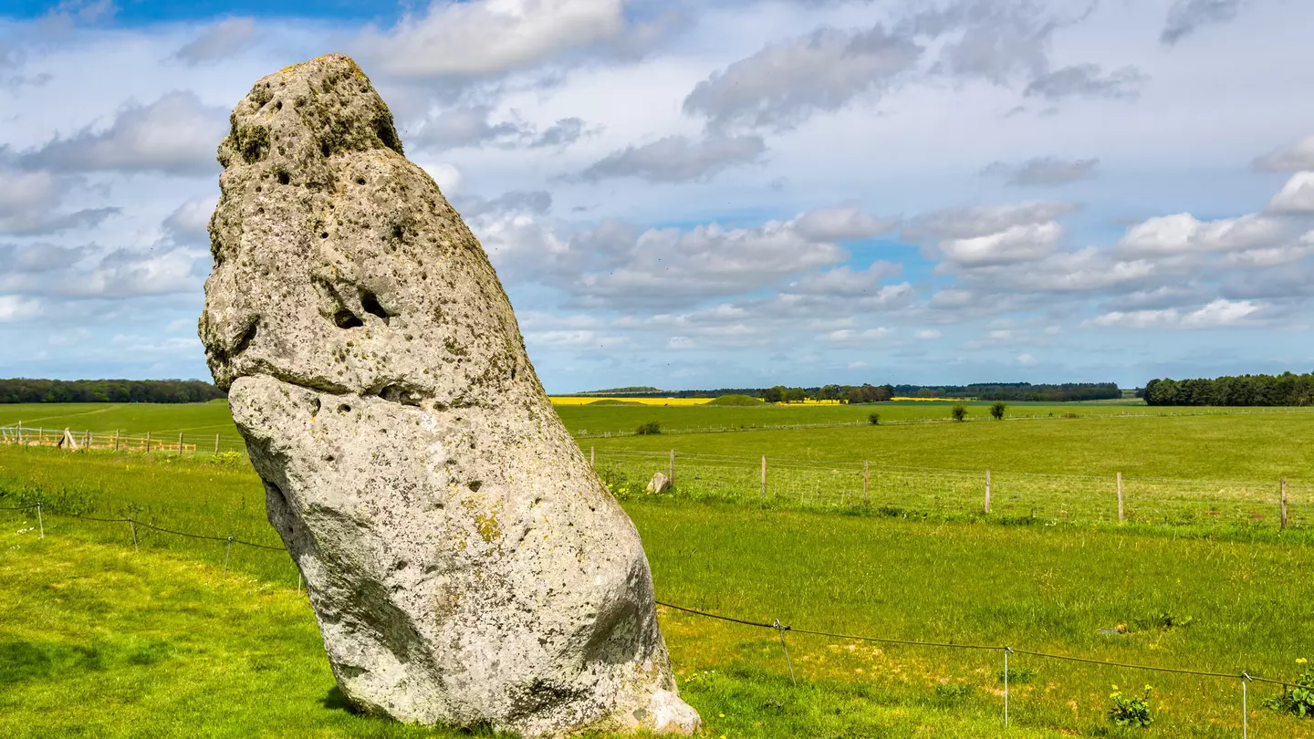 A giant stone stands alone, surrounded by green farmland. The stone leans slightly to the left