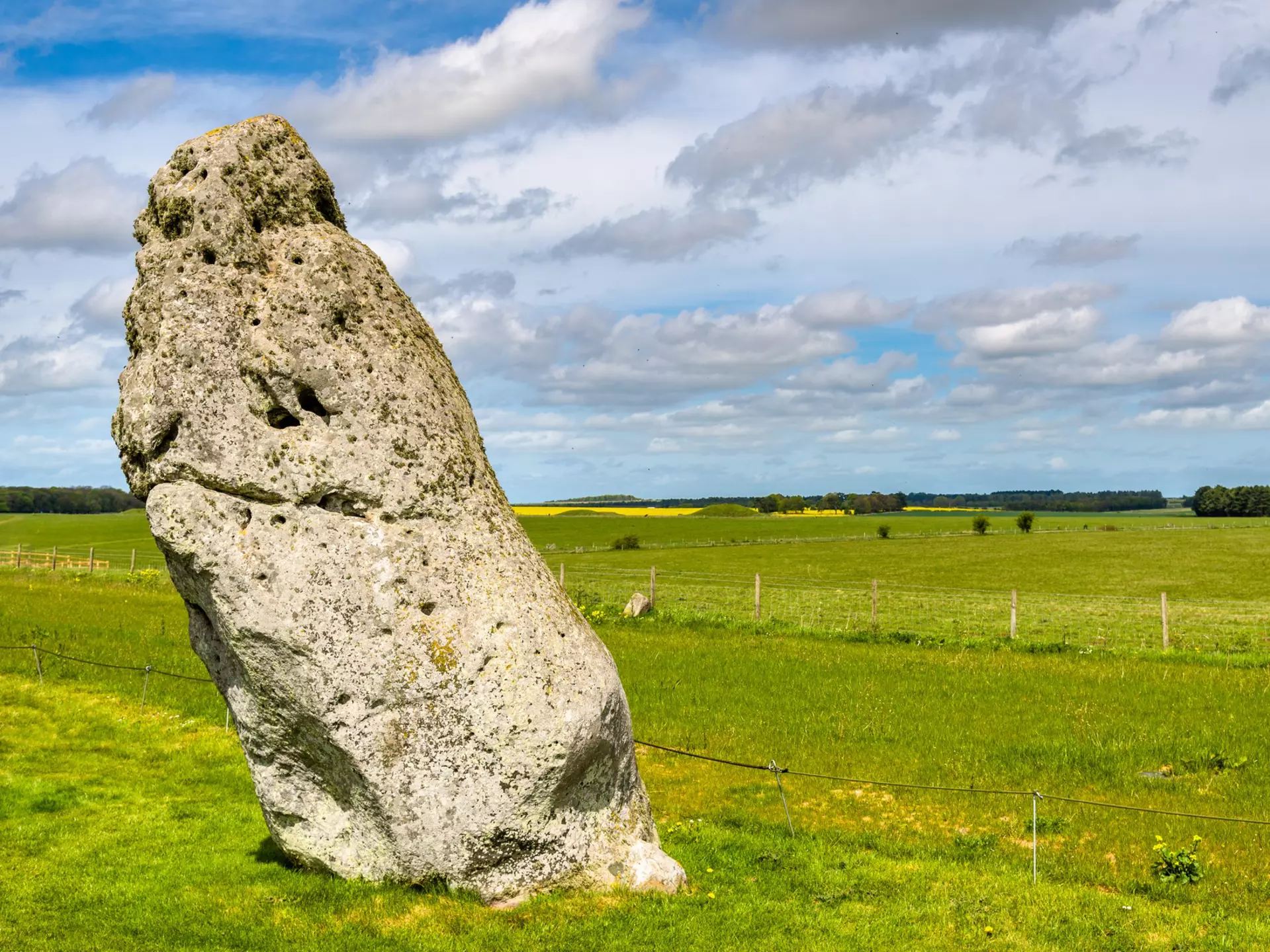 A giant stone stands alone, surrounded by green farmland. The stone leans slightly to the left