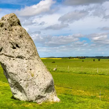 A giant stone stands alone, surrounded by green farmland. The stone leans slightly to the left