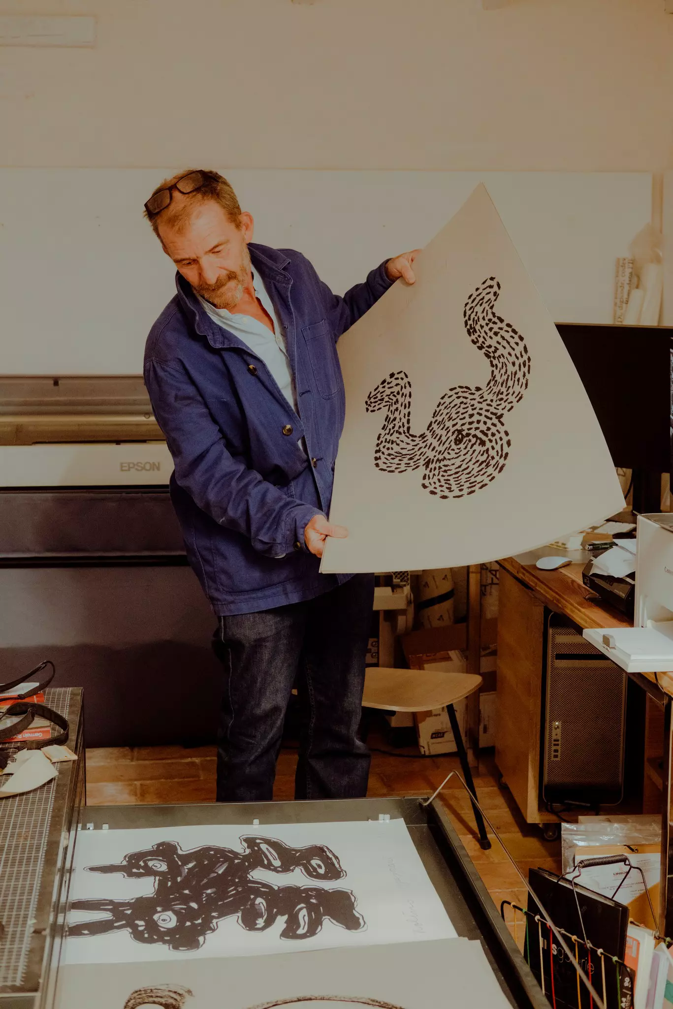 A person holds up a large print in an art studio.