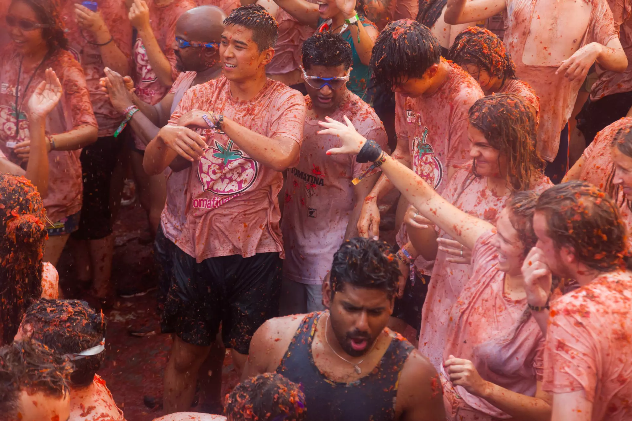 A crowd of men in pink t-shirts amongst a throng of people throwing tomatoes