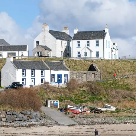 A woman walks with her two dogs near white houses by the shore at the southwest tip of Islay, Scotland
