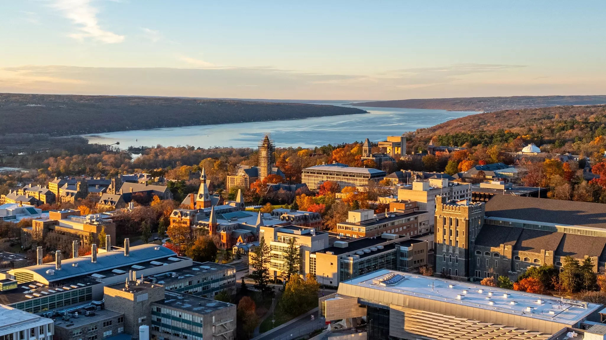 Aerial view of a city with stone and brick builings on an autumnal, sunny day with a large lake and low hills in the distance.