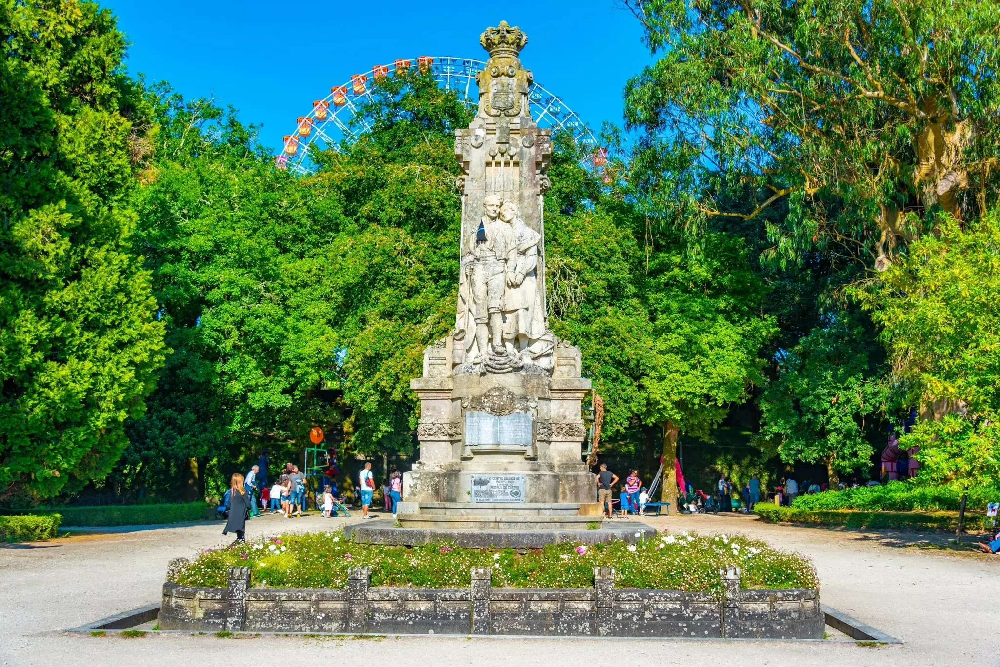A stone statue in the middle of a park square on a sunny day.
