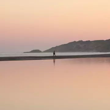 A woman walks along a sunset beach.